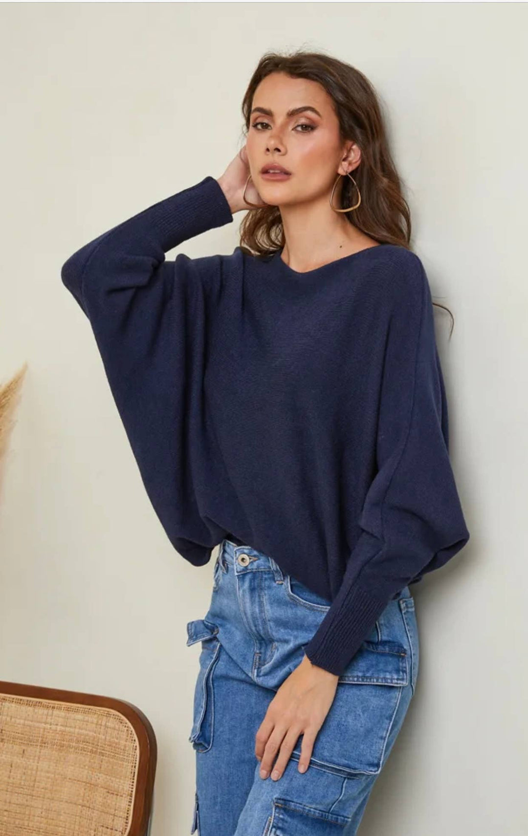 Woman wearing a navy sweater and blue jeans against a beige wall.