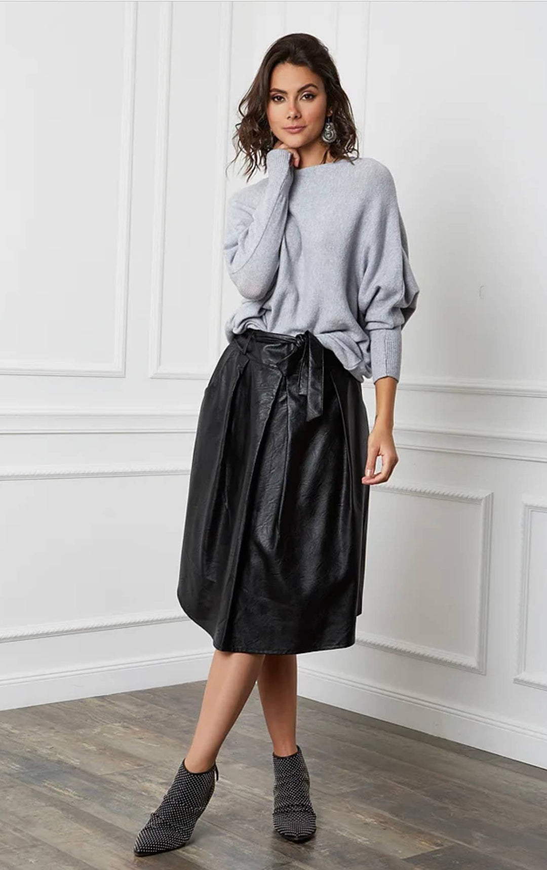 Woman wearing a gray sweater and black skirt in a minimalistic room.