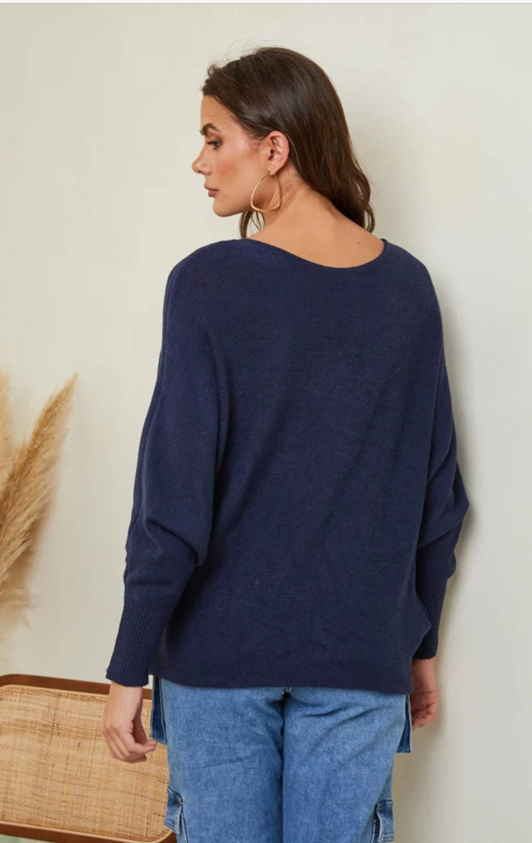 Woman wearing a navy sweater and blue jeans against a neutral background