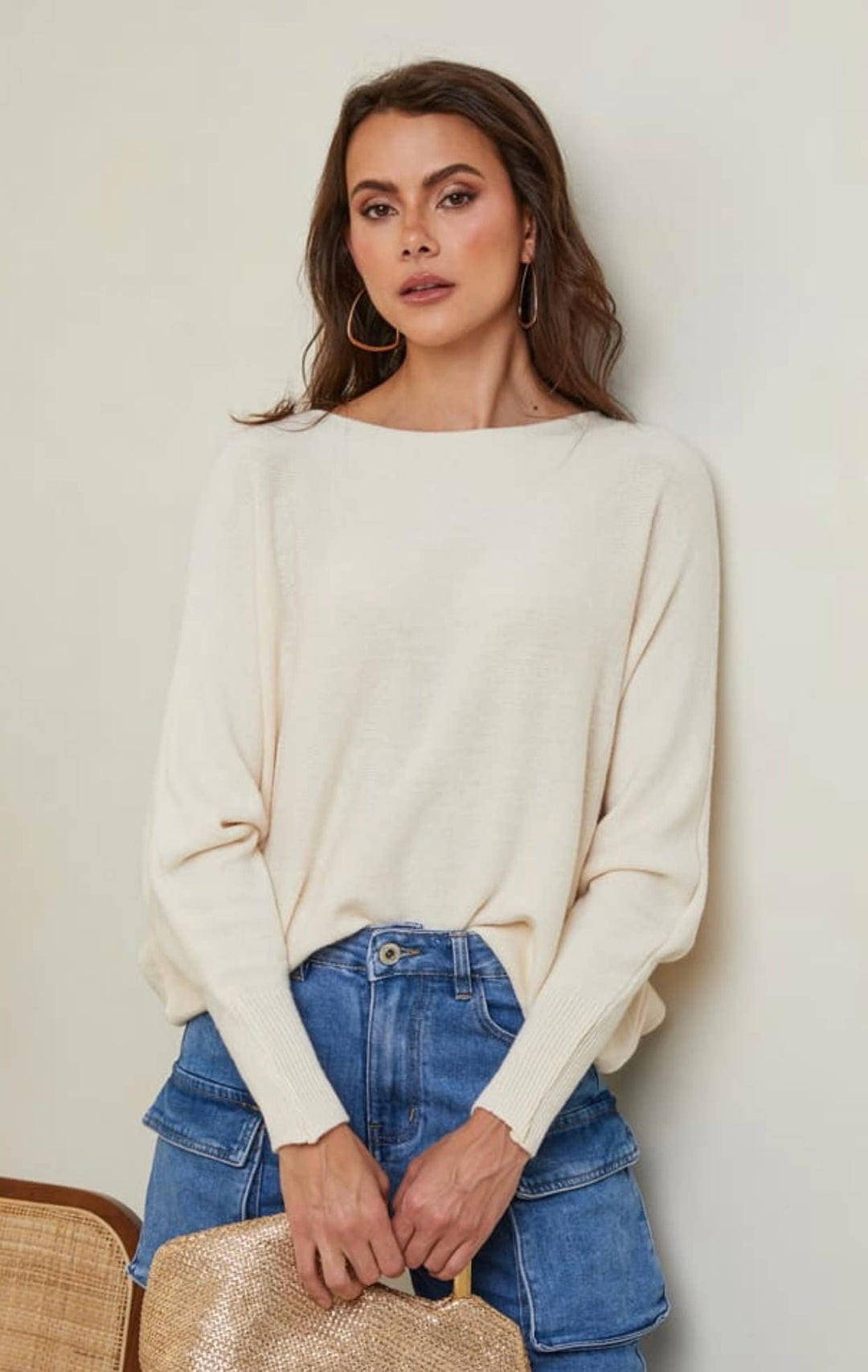 Woman wearing a cream sweater and blue jeans against a plain background