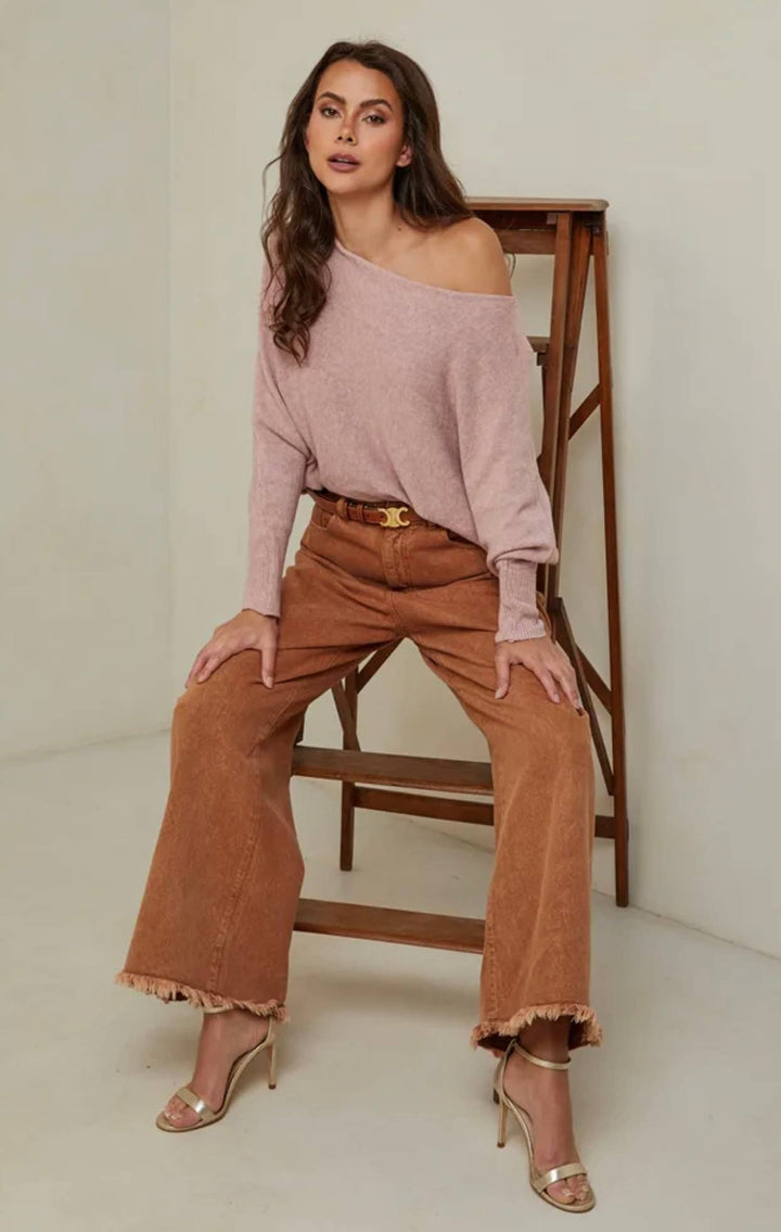 Woman wearing a pink off-shoulder top and brown wide-leg pants sitting on a wooden chair.