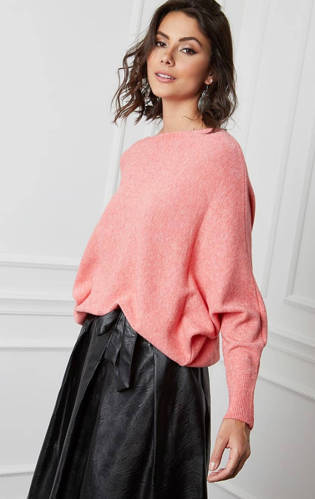 Woman wearing a pink sweater and black skirt against a white background