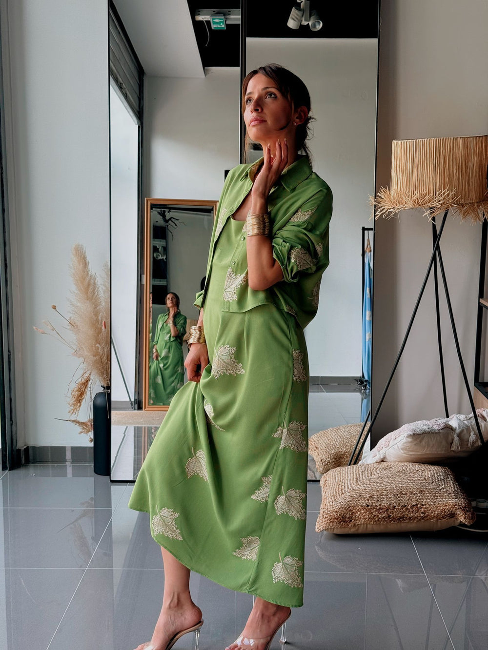 Woman in a green dress with floral patterns standing in a modern interior setting.