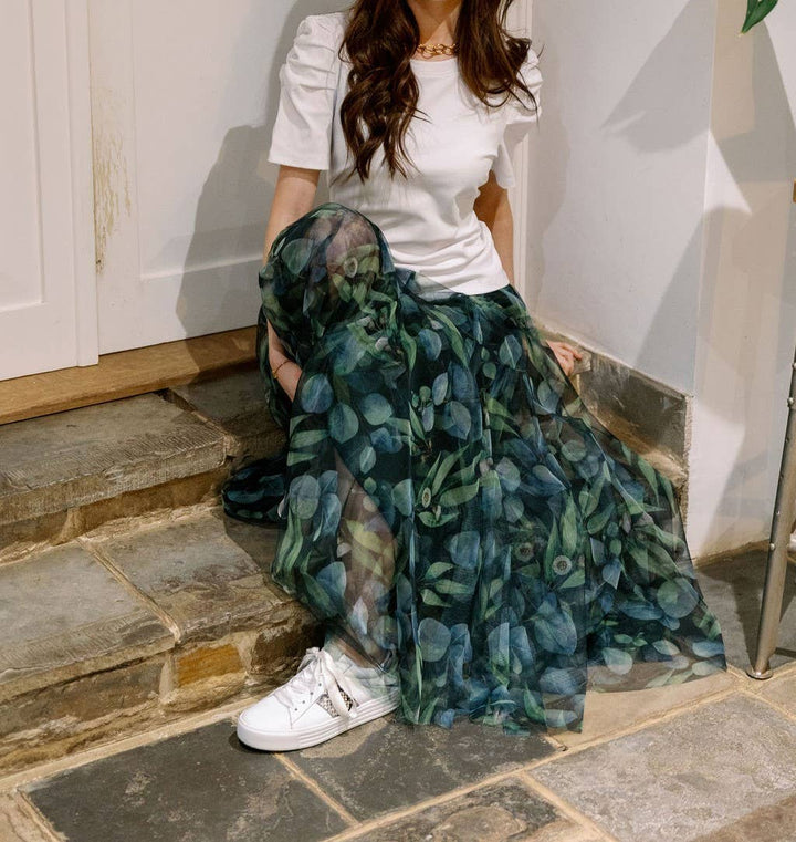 Person wearing a white top and floral skirt on stone steps.