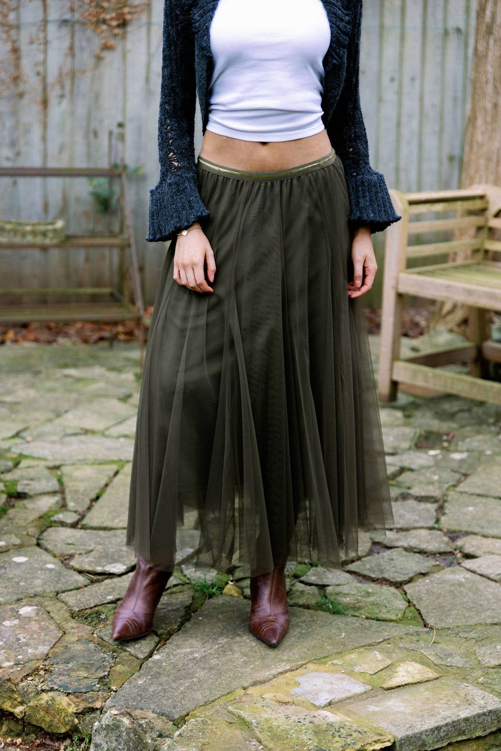 Person wearing a white top, dark jacket, and green tulle skirt on a stone patio.