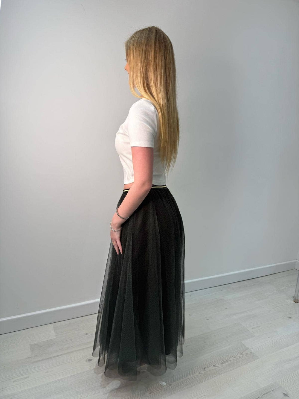 Woman wearing a white top and black tulle skirt against a plain white wall.