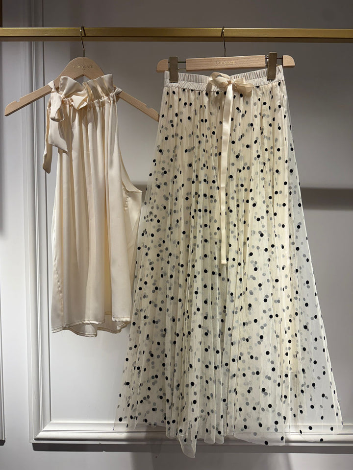Two dresses, one beige and one with black polka dots, hanging on a rack.