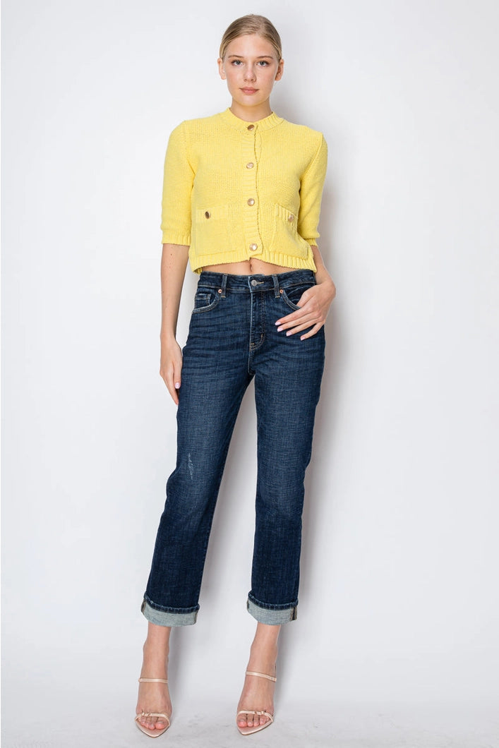 Woman wearing a yellow cropped cardigan and blue jeans on a white background