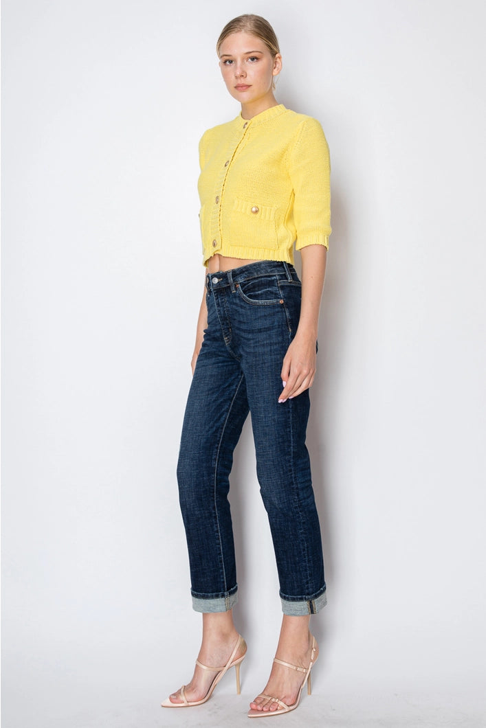 Woman wearing a yellow cropped cardigan and dark blue jeans on a white background
