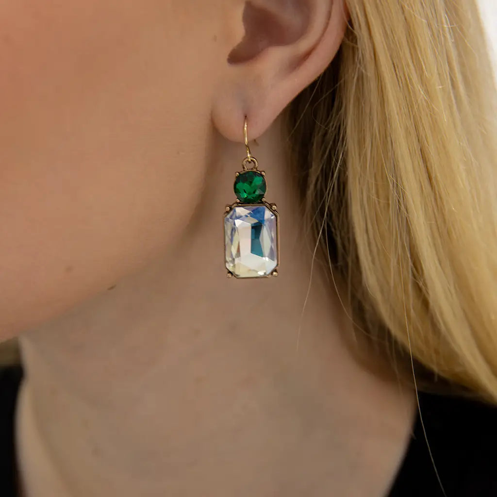 Close-up of a person wearing an earring with a green gemstone and clear crystal.