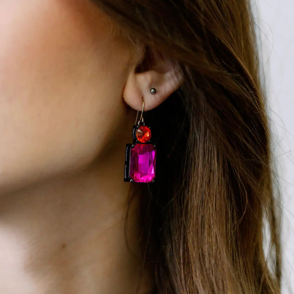 Close-up of a person wearing a colorful earring with a pink gemstone.