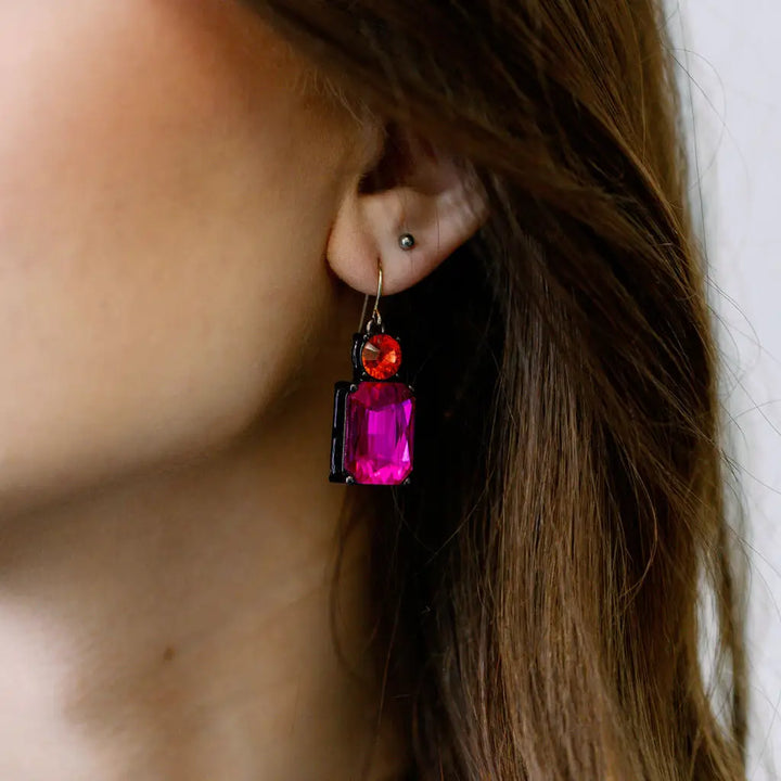 Close-up of a person wearing a colorful earring with a pink gemstone.