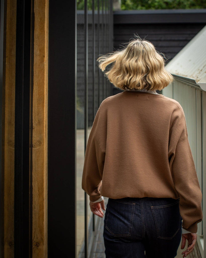 Person wearing a brown sweater and dark jeans walking away from the camera.
