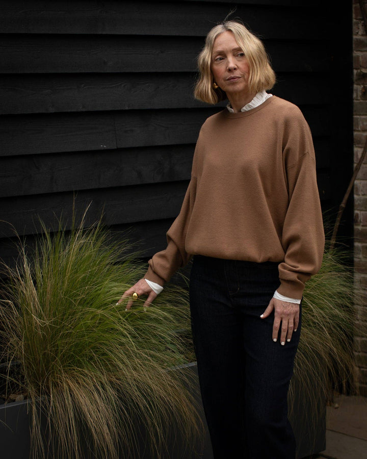 Woman in a brown sweater standing outdoors next to plants