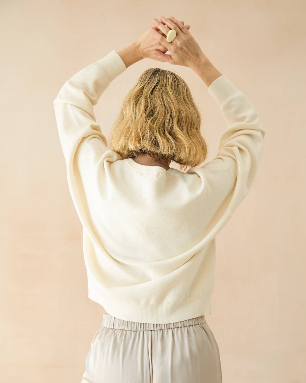 Person wearing a white sweater against a light pink background