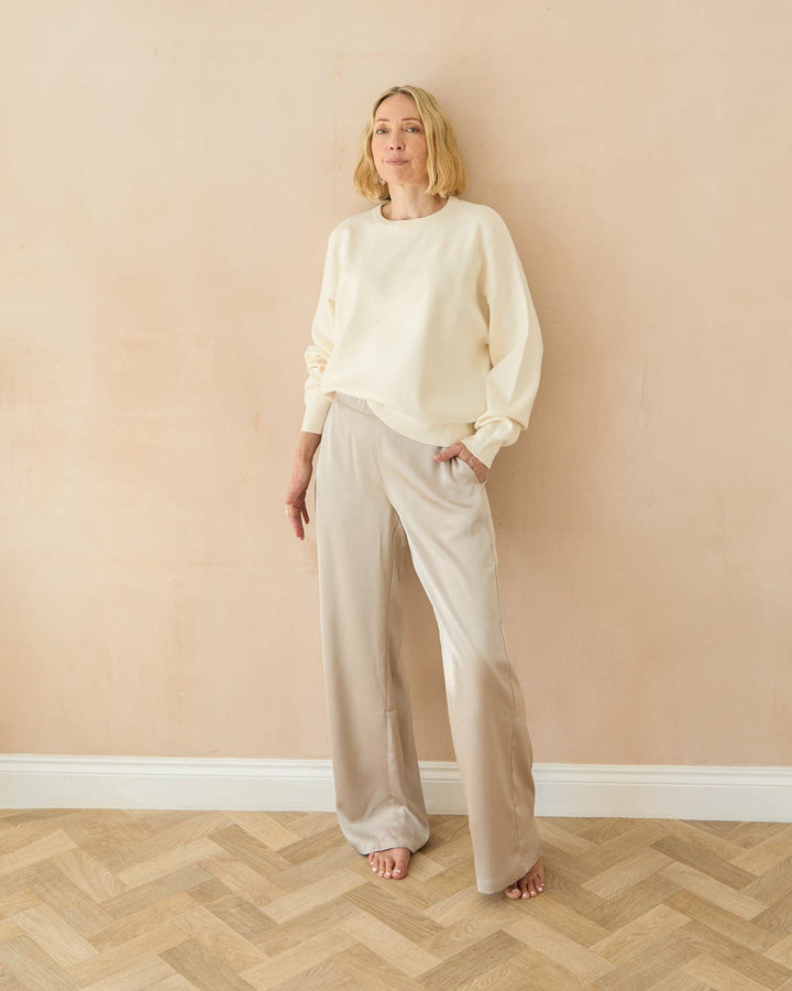 Woman wearing a white outfit standing against a beige wall.