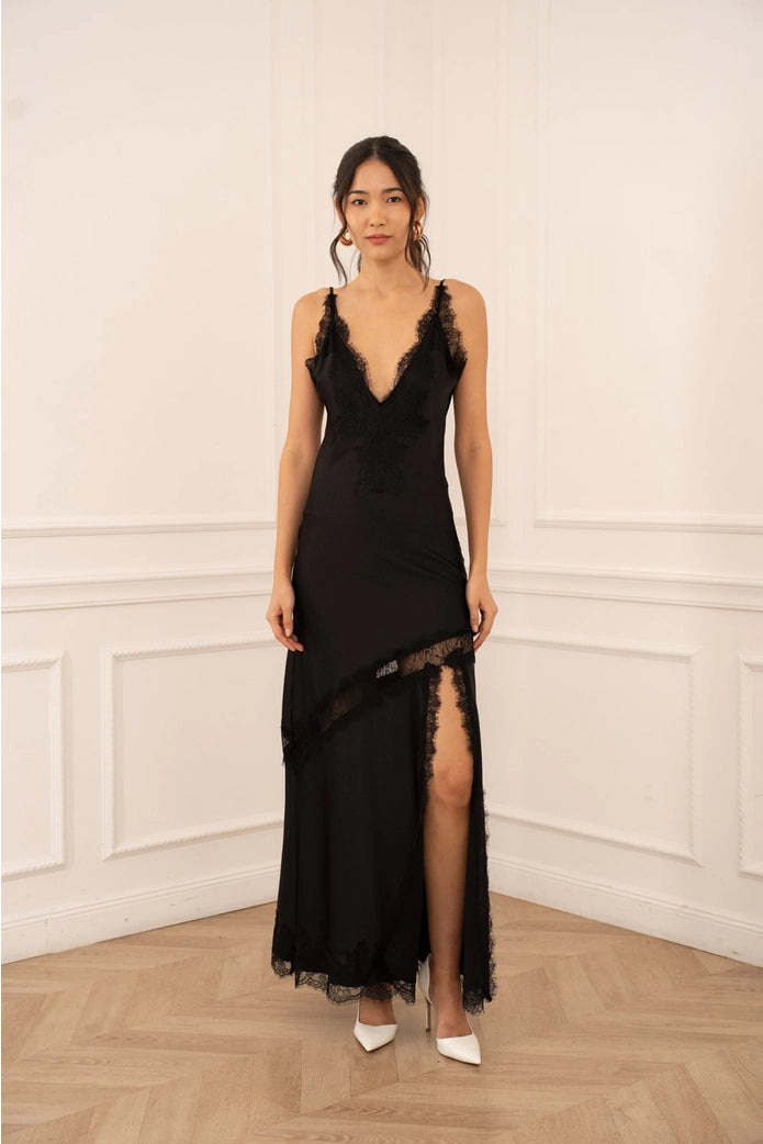Woman wearing a black lace dress with a slit in a room with white walls and wooden floor.