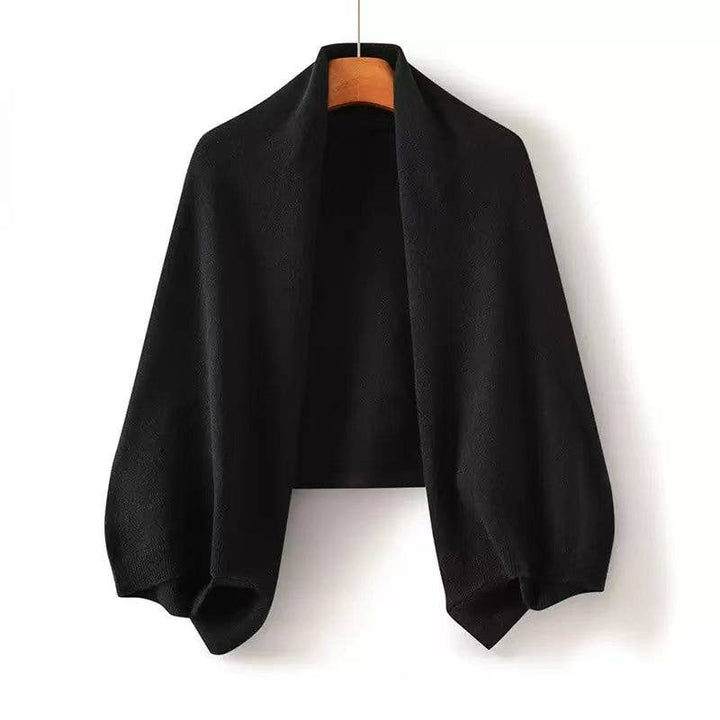 Black poncho on a hanger against a white background