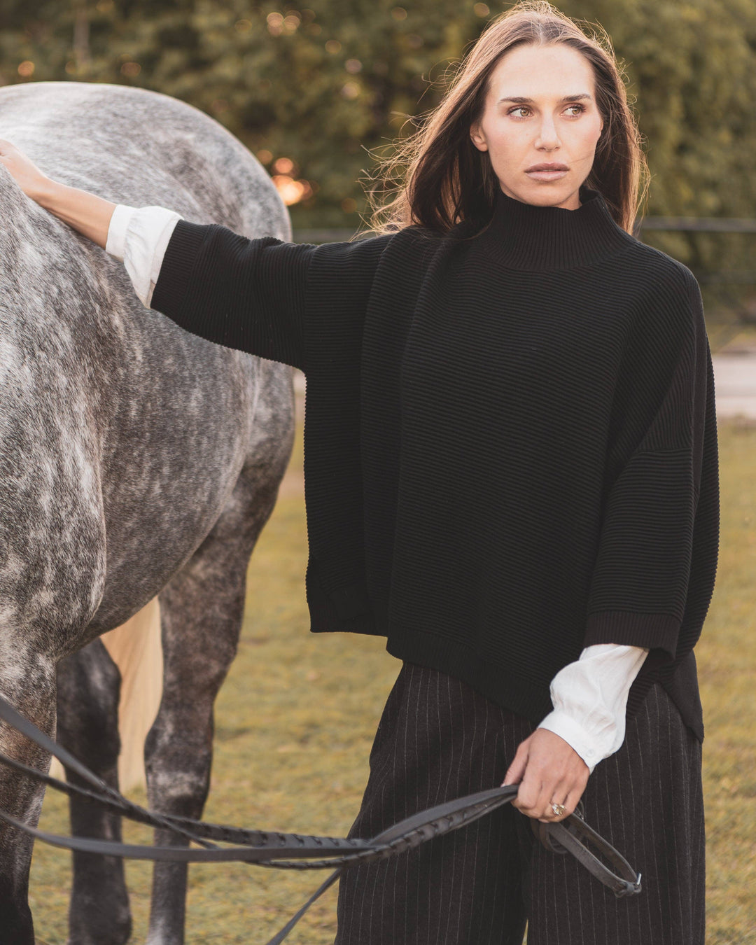 Woman in a black sweater standing next to a horse in an outdoor setting
