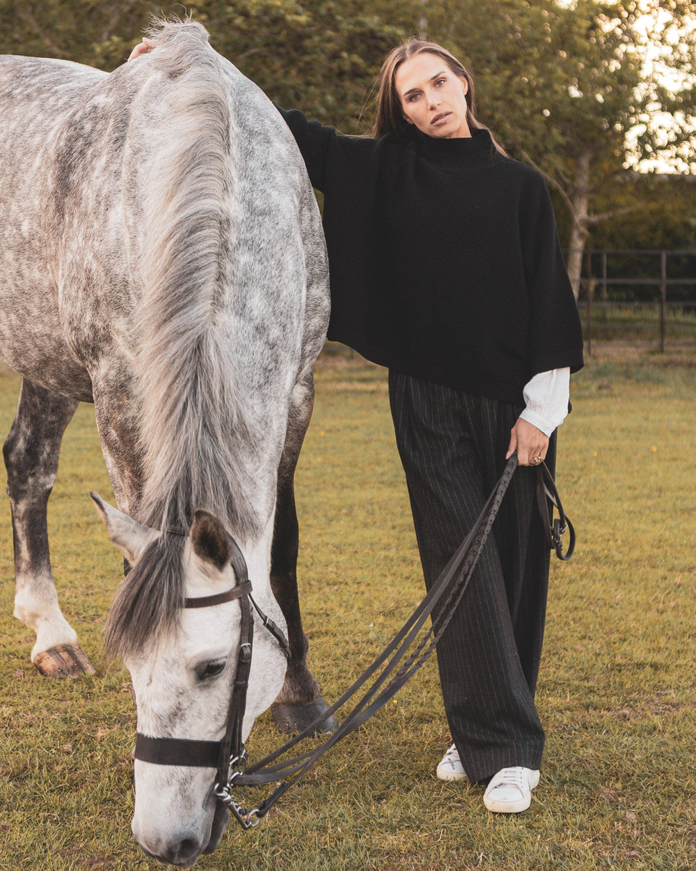 Woman in black outfit standing next to a gray horse in an outdoor setting