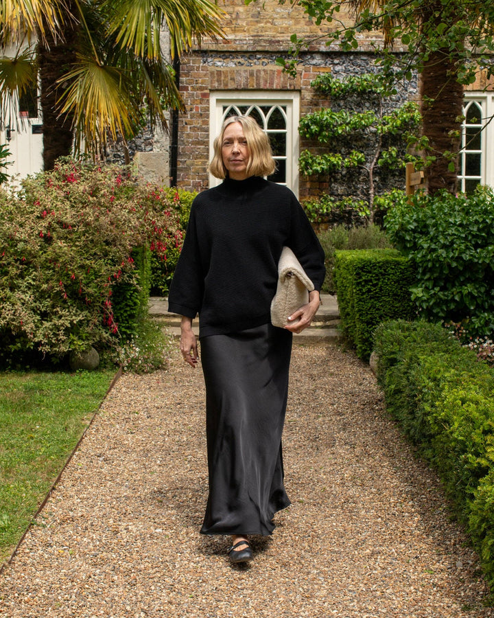 Woman in black outfit holding a clutch in a garden setting