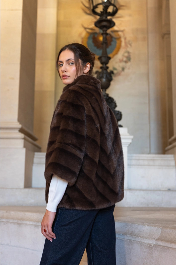 Woman wearing a brown fur coat standing on a staircase with classical architecture.