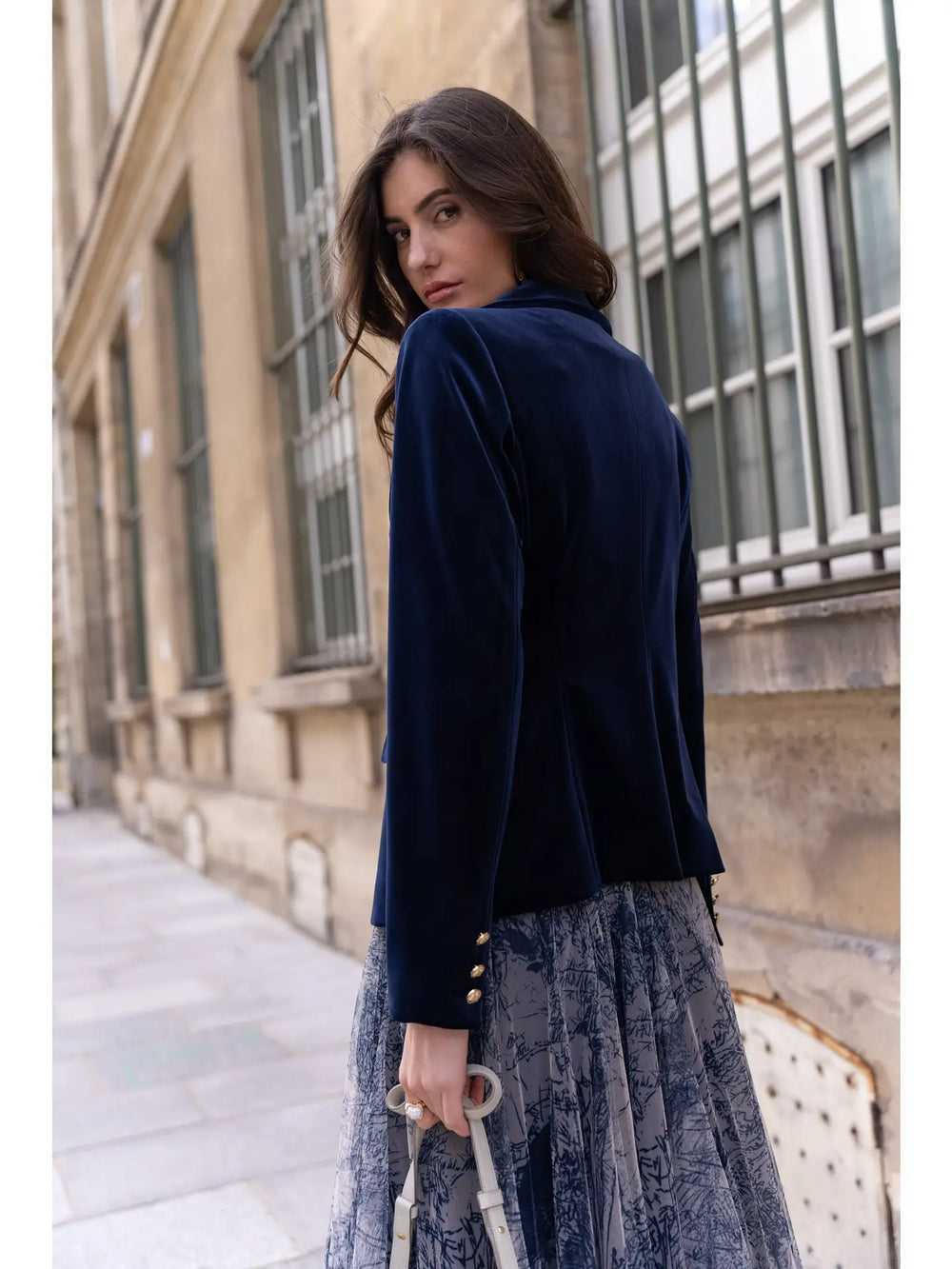 Woman wearing a navy blazer and lace dress standing on a street.
