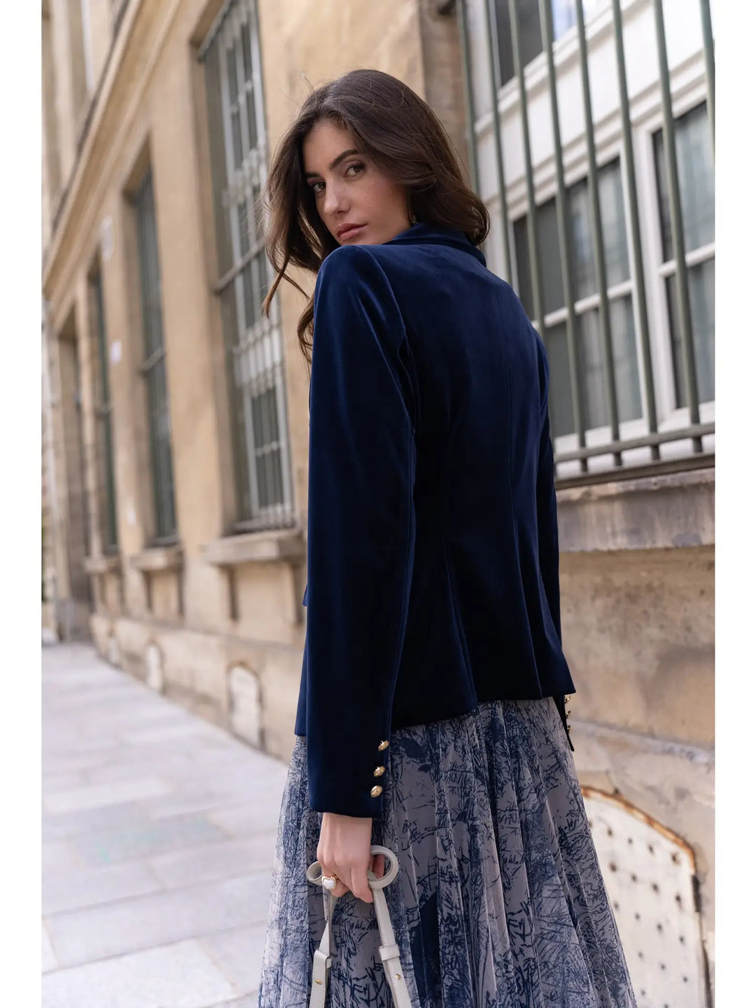 Woman wearing a navy blazer and lace dress standing on a street.