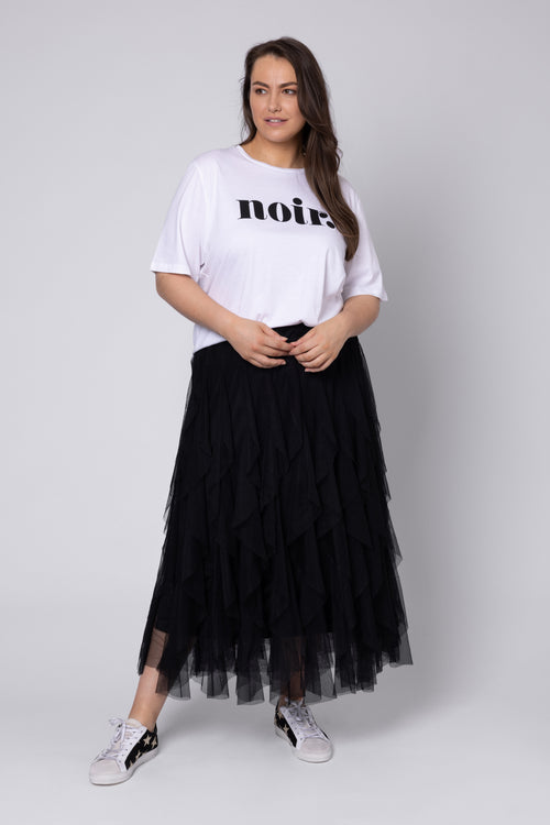 Woman wearing a white t-shirt with text and a black tulle skirt on a plain background