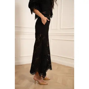 Person wearing a black lace outfit against a white wall.
