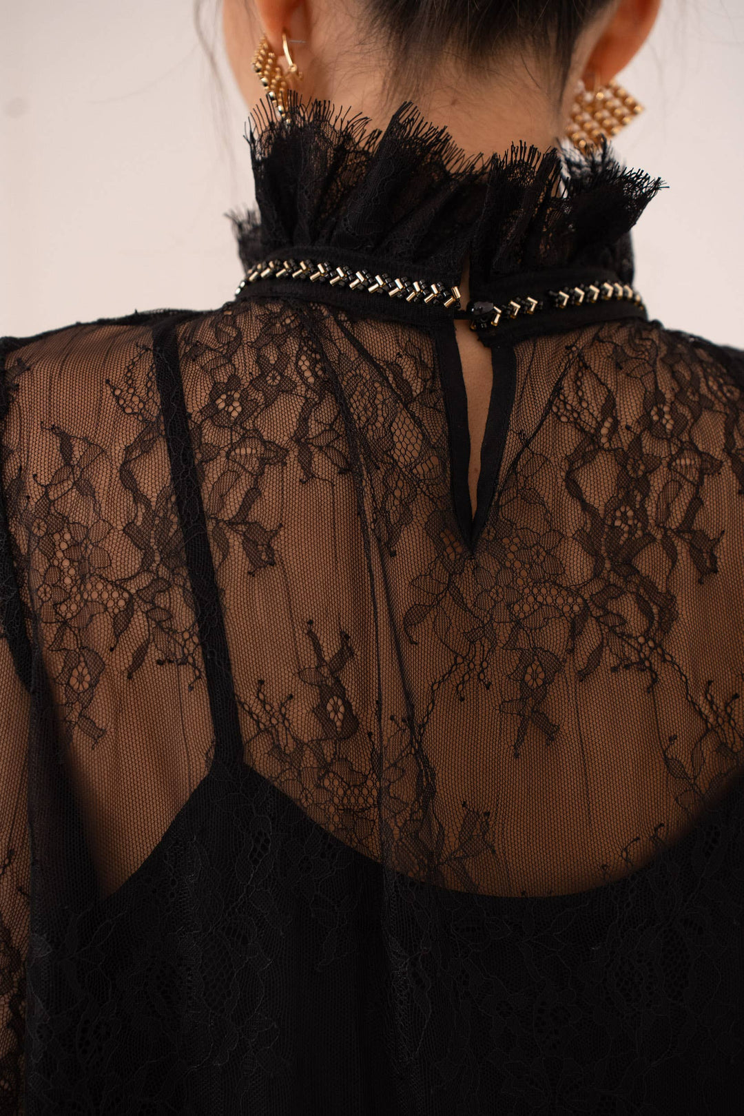 Black lace top with decorative straps and embellishments on a neutral background