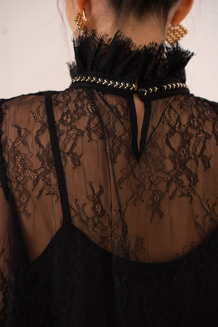 Black lace top with decorative straps and embellishments on a neutral background