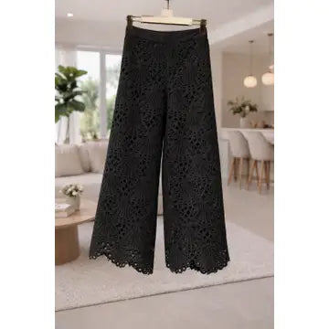 Black lace pants hanging in a room with a couch and plants.