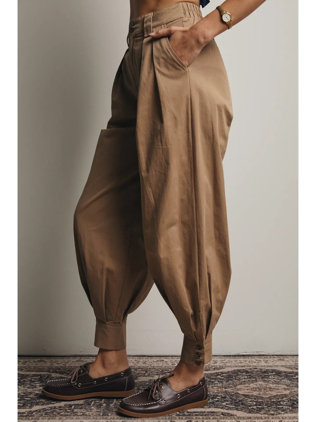 Person wearing brown harem pants and dark shoes on a neutral background