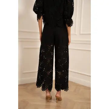 Person wearing a black lace outfit against a white wall.